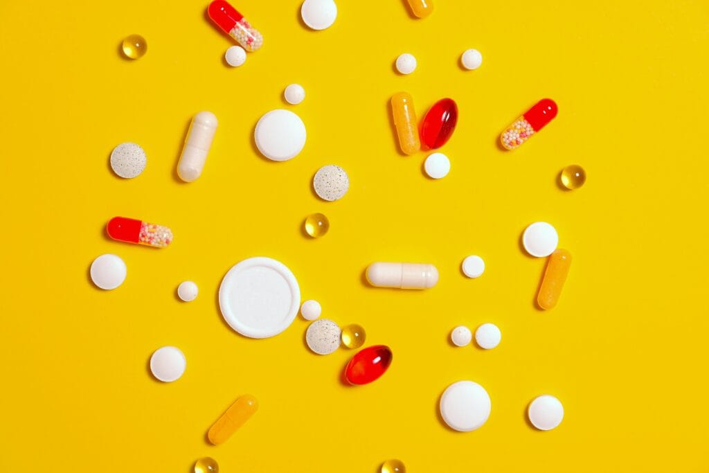 A variety of pills and capsules scattered on a vibrant yellow backdrop, emphasizing health and medicine.