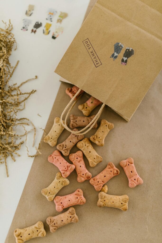 Colorful bone-shaped dog treats spill from a paper bag labeled 'thank you'.