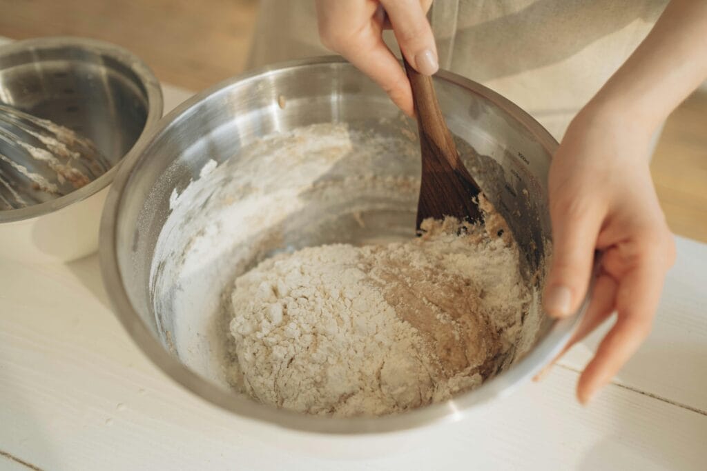 Hands mixing dough with a wooden spatula in a stainless steel bowl, perfect for baking themes.